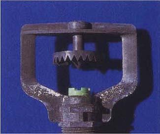 Above, the nozzle of a spray sprinkler directs water over the serrated deflector plate into multiple horizontal jets of water.